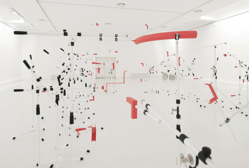 History in the MakingRauminstallationLackierte Mikrofonständer, pulverbeschichtete Metallelemente, RohrschellenEngländerbau Vaduz, Kunstraum Liechtenstein2013Pressetext:Alexandra Berlinger und Wolfgang Fiel sind unter dem Namen tat ort in den Bereichen Bildende Kunst, Architektur und Urbanismus tätig. Nach über einer Dekade des gemeinsamen Arbeitens haben sie nun für den Kunstraum Engländerbau unter dem Titel History in the Making eine Rauminstallation entwickelt, die sie als retroaktives Manifest ihrer künstlerischen Praxis verstehen. Ein häufig wiederkehrendes Motiv ist dabei ihre Auseinandersetzung mit der temporären Formation kollektiver Prozesse und den dabei ausgetragenen Konflikten. In vielen Fällen bleibt die Arbeit des Künstlerduos auf die Zeit beschränkt, die sie vor Ort verbringen und dort oft mehrere Wochen in einen gegebenen Kontext eintauchen. Dass selbst die Konstitution des physischen Raums davon nicht unberührt bleibt, zeigt sich nicht zuletzt an den temporären ‚Apparaturen‘, die Berlinger und Fiel für ihre Interventionen konstruieren.&nbsp;Sie beschäftigen sich dabei unter anderem mit der Frage, inwieweit diese Strukturen potentiell auf unsichtbare/verborgene Prozesse verweisen können und dabei zwischen eigenständiger Form und funktionalem Hilfsmittel changieren. Im Gegensatz zu den unterschiedlichsten Objekten und Materialien die in ihren Arbeiten zum Einsatz kommen, verstehen sie die geschaffenen Environments als Katalysatoren von Prozessen, die im Idealfall den Zeitraum der ursprünglichen Inszenierung überdauern.&nbsp;Wichtiger Bestandteil ihrer Werkdokumentation ist die minutiöse digitale Archivierung der eingesetzten Mittel, die ihnen erlaubt, die eigene Entwicklung retrospektiv als vielschichtige Sequenz diskreter Ereignisse zu begreifen, deren ‚Spuren‘ einen Namen tragen, denen sie die Treue halten.&nbsp;Die digitalen Ressourcen ausgewählter Arbeiten werden für die Ausstellung zu einer imaginären Großform innerhalb der räumlichen Begrenzungen des Engländerbaus assembliert, die aber lediglich mittelbar angezeigt, vorgebracht, eingefasst oder abgetastet wird. Die zu diesem Zweck verwendeten handelsüblichen Mikrofonstative sind die justierbaren Träger eines jeweils an deren Ausleger montierten Passstücks, das der Kontur der imaginären Skulptur an einer bestimmten Stelle nachgeformt ist, und sich somit in ihrer Gesamtheit zu einem räumlichen Ensemble verdichten. Die Installation ist die physische Manifestation einer historischen Fiktion.&nbsp;Die zur Ausstellung erscheinende Publikation dokumentiert die digitalen Ressourcen der ausgewählten Projekte und liefert somit den Bauplan zur räumlichen Inszenierung.Fotos Barbara Bühler, ©tat ort(tat ort)